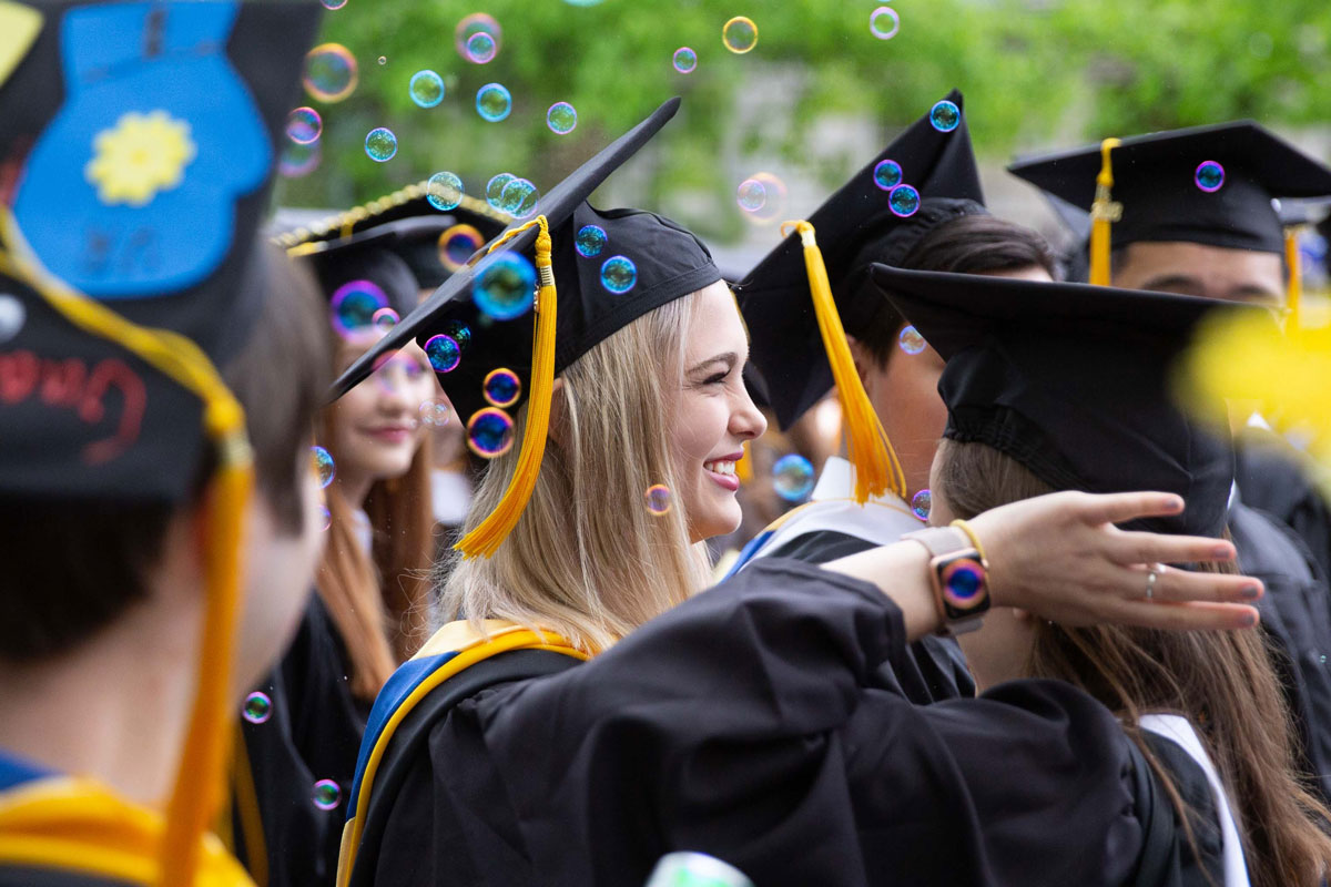 Graduates in caps and gowns celebrate with bubbles floating in the air at the University of Rochester commencement ceremony.