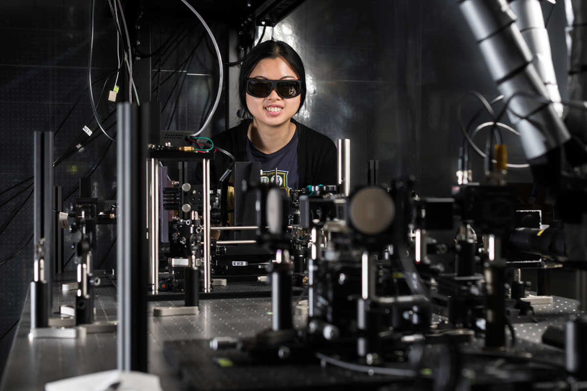A University of Rochester student wearing sunglasses operates a machine in a laboratory setting.