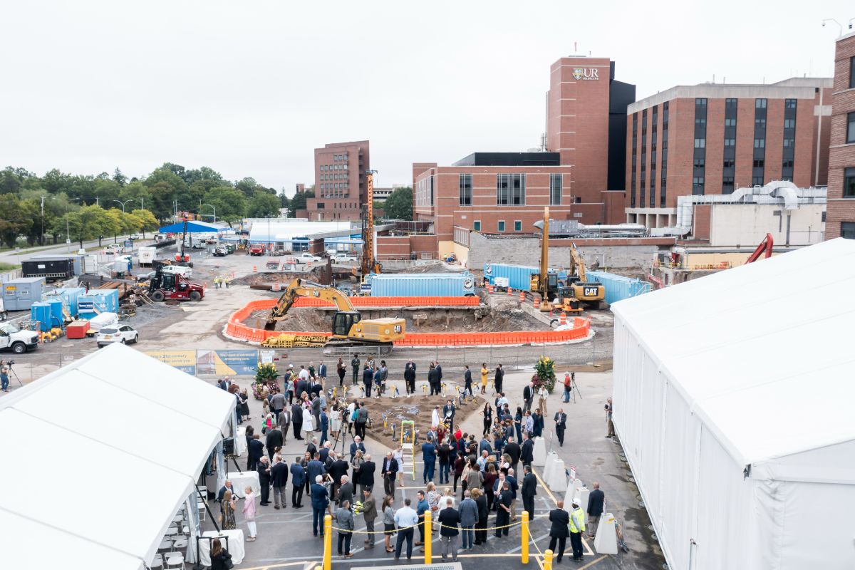 A diverse crowd gathers at the University of Rochester for a groundbreaking event at a construction site.