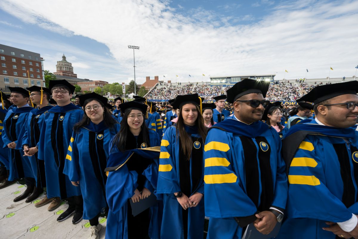 A group of University of Rochester graduates poses together in front of a stadium, celebrating their academic achievements.