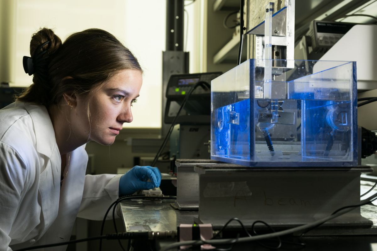A woman in a lab coat examines a blue object in a research setting at the University of Rochester.