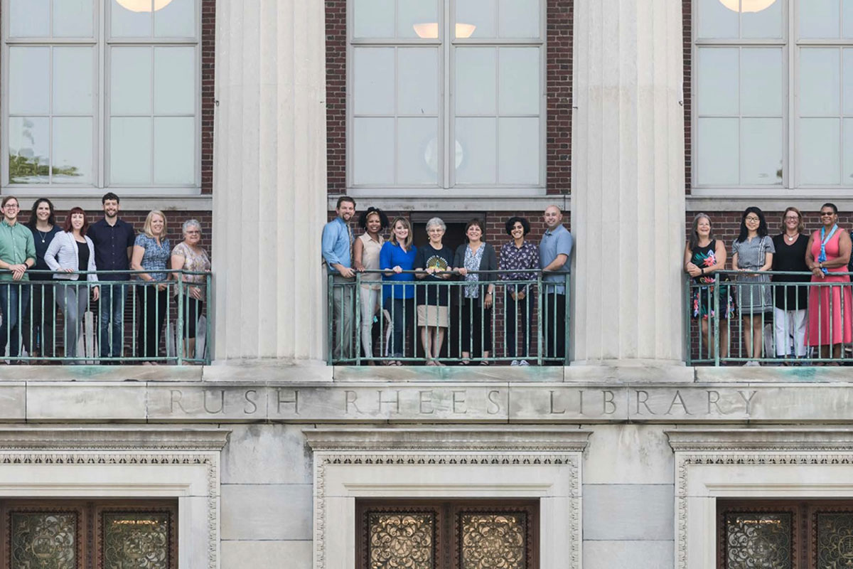 A group of University of Rochester employees stands together on a building balcony, enjoying the view and each other's company.
